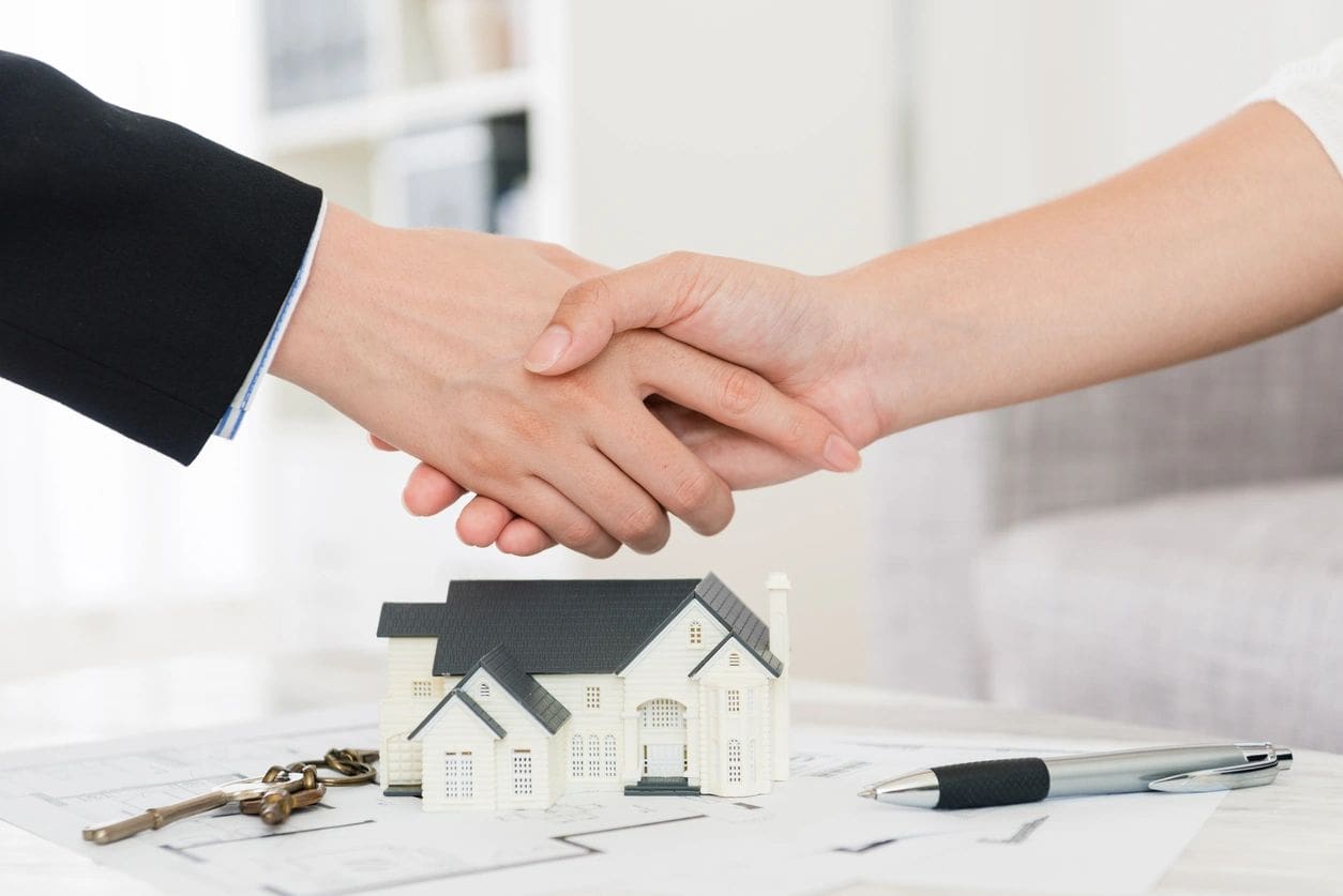 Two hands shaking over a house model.