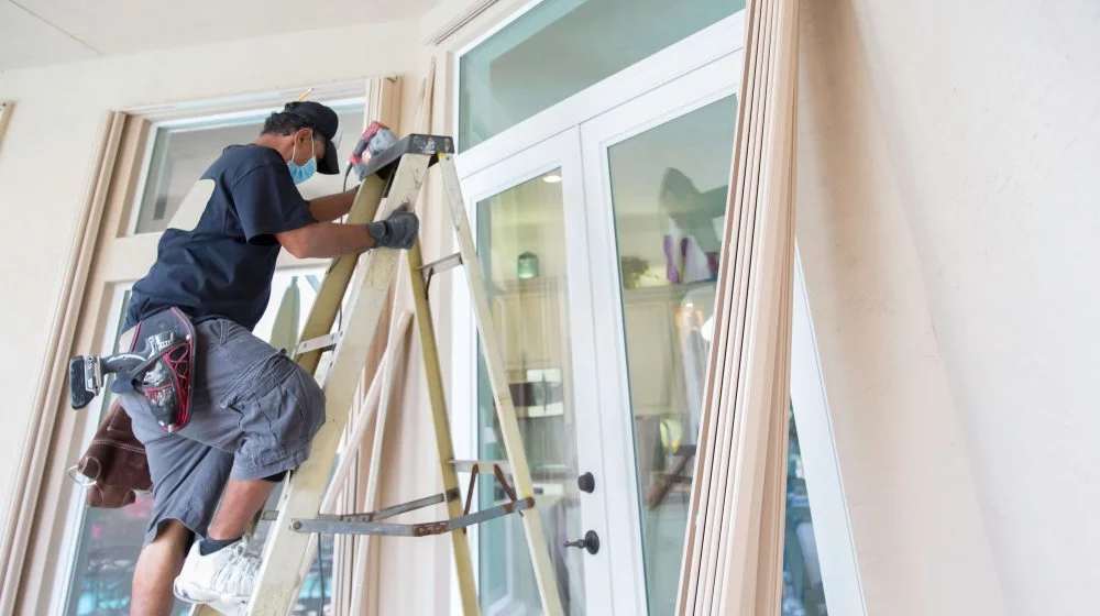 Man on ladder installing window blinds.